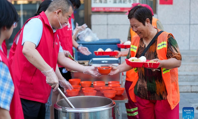 Zhang Changqin (L) delivers soup to a sanitation worker in Yanhu District, Yuncheng City, north China's Shanxi Province, July 8, 2026. Ten years ago, Zhang Changqin, head of the volunteer association in Yanhu District, Yuncheng City, Shanxi Province, saw a sanitation worker eating a hard and cold bun with nothing but cold water on a chilly winter morning. The scene struck him deeply. At that moment, he decided to start a public welfare project -- providing free breakfasts for street cleaners.

