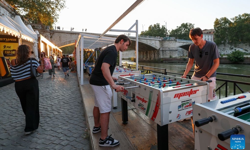 Tourists play table football game along the Tiber River in Rome, Italy, July 12, 2026. The 24th edition of Along the Tiber Rome event is held here along the banks of the Tiber and will run until the end of August. It has become a popular summer event featuring culture, music and gastronomy. (Xinhua/Wang Kaiyan)