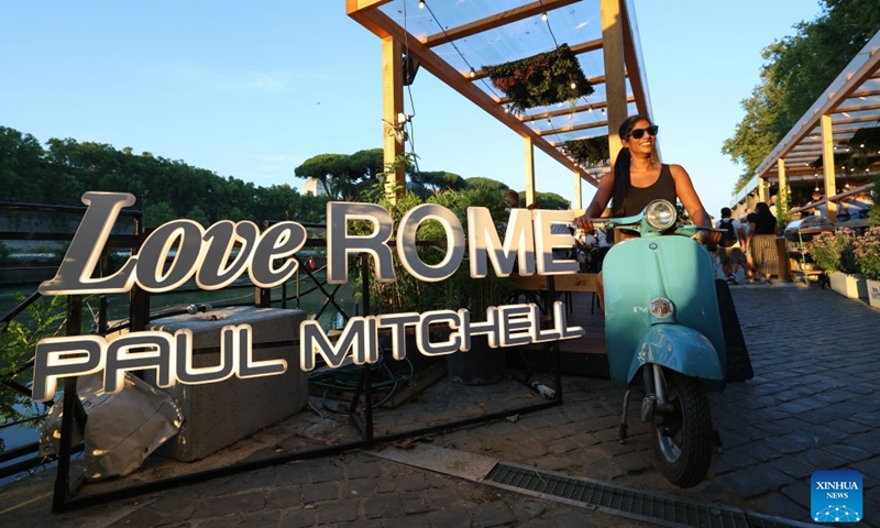 A woman poses for photos with the slogan Love Rome along the Tiber River in Rome, Italy, July 12, 2026. The 24th edition of Along the Tiber Rome event is held here along the banks of the Tiber and will run until the end of August. It has become a popular summer event featuring culture, music and gastronomy. (Xinhua/Wang Kaiyan)