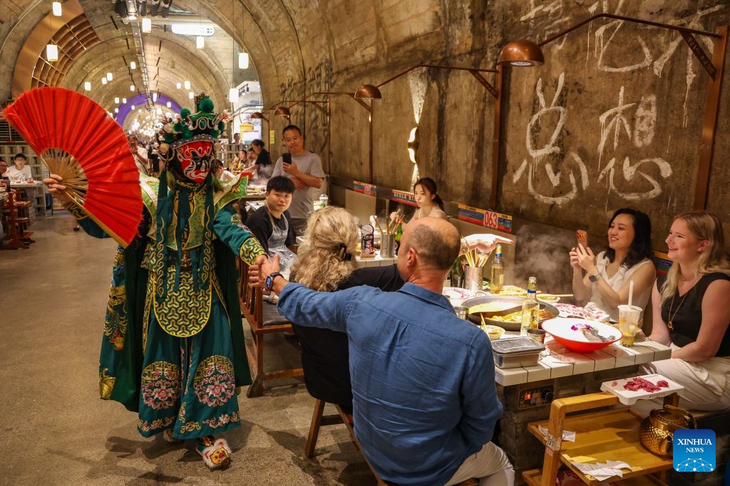 A foreign tourist interacts with a Sichuan Opera performer at a hotpot restaurant housed in a former underground air-raid shelter in Liangjiang New Area of southwest China's Chongqing Municipality, July 10, 2026. Since the beginning of this year, inbound and outbound passenger traffic at Chongqing Jiangbei International Airport has continued to grow, with a significant increase in foreign passenger traffic. In the first half of 2026, the airport handled more than 1.48 million inbound and outbound passenger trips, up 39.5 percent year on year. (Photo: Xinhua)