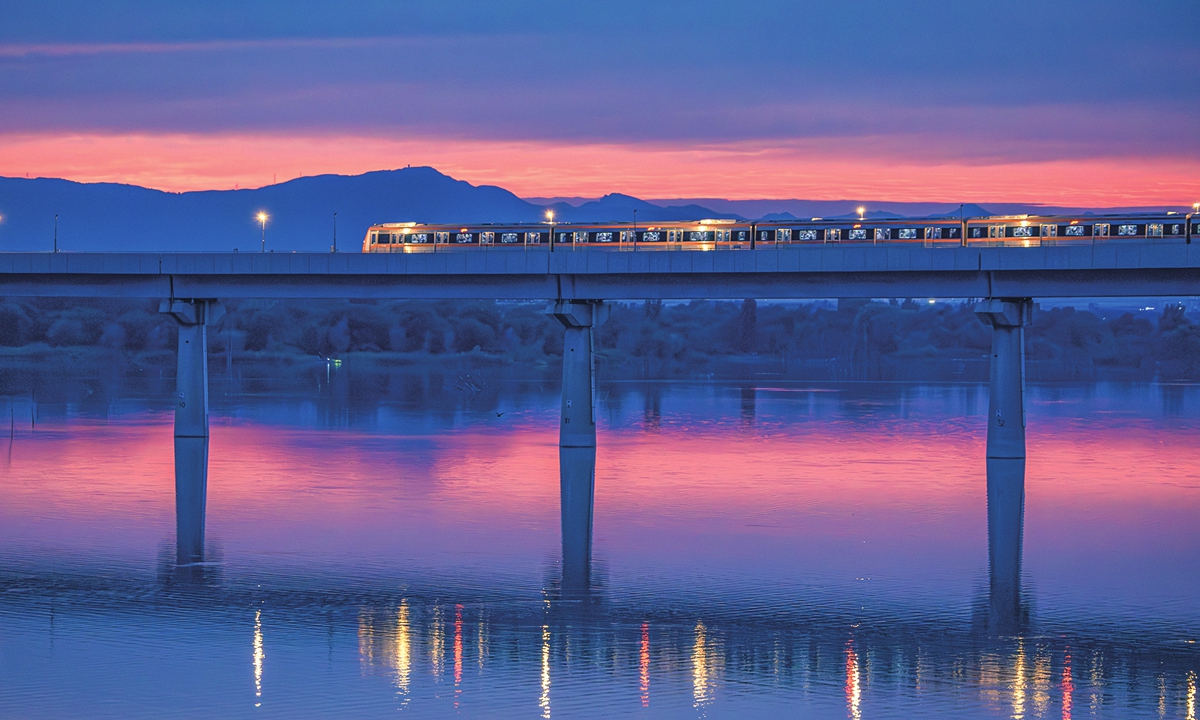 A metro train on Beijing's Fangshan Line crosses the Yongding River Bridge amid a glowing sunset in a park in Beijing on July 14, 2026. The clear evening sky appeared following days of frequent rains in the Chinese capital as temperatures climbed into 34 C to 36 C from July 13 to July 14, per weather.com. Photo: Li Hao/GT