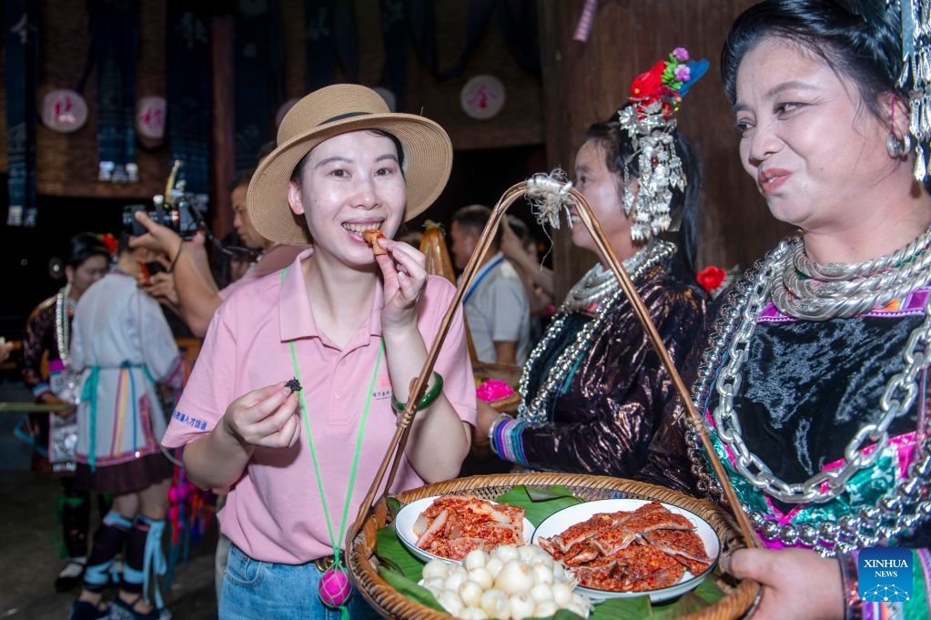 A tourist tries local specialty foods during a musical event in Congjiang County of southwest China's Guizhou Province, July 12, 2026. The event featuring performing arts of the Dong ethnic group and local specialty foods was held here on Sunday, attracting hundreds of tourists. (Photo: Xinhua)