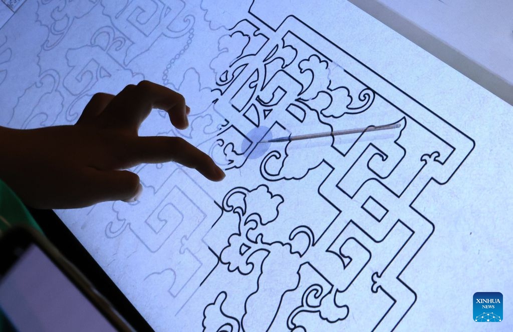 A visitor tries a simulated handcraft experience during A Garden Within: An Immersive Light and Shadow Exhibition of the Qianlong Garden at National Museum of Classic Books in Beijing, capital of China, July 14, 2026. The exhibition, which features multiple immersive scenarios and interactive installations, is held here from July 9 to Dec. 6. The Qianlong Garden, also known as the Garden of the Palace of Tranquil Longevity, was built by Emperor Qianlong (1711-1799) of Qing Dynasty (1644-1911) as a private retreat for his later years in the Forbidden City, or today's Palace Museum. (Photo: Xinhua)