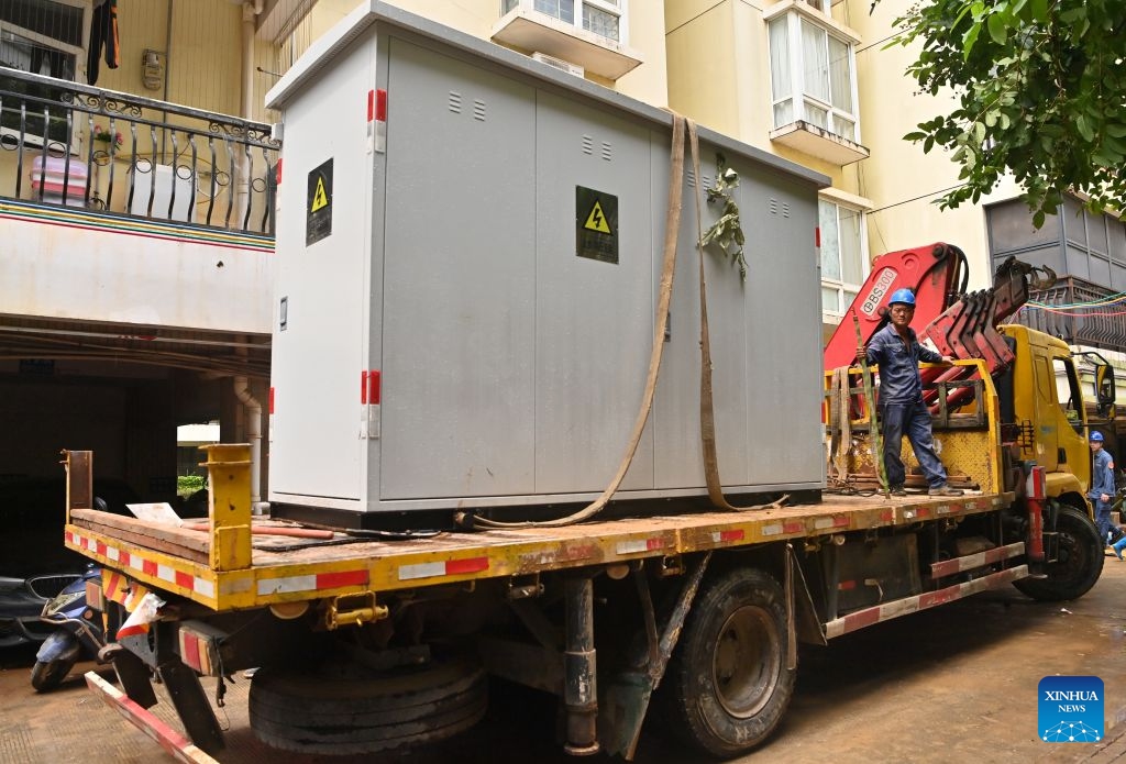 Staff members bring power device for replacement into a residential compound in Guigang City, south China's Guangxi Zhuang Autonomous Region, July 14, 2026. The power supplier in Guigang has mobilized all hands available to restore power supply as flooding inflicted by typhoon Maysak subsides in the city. (Photo: Xinhua)