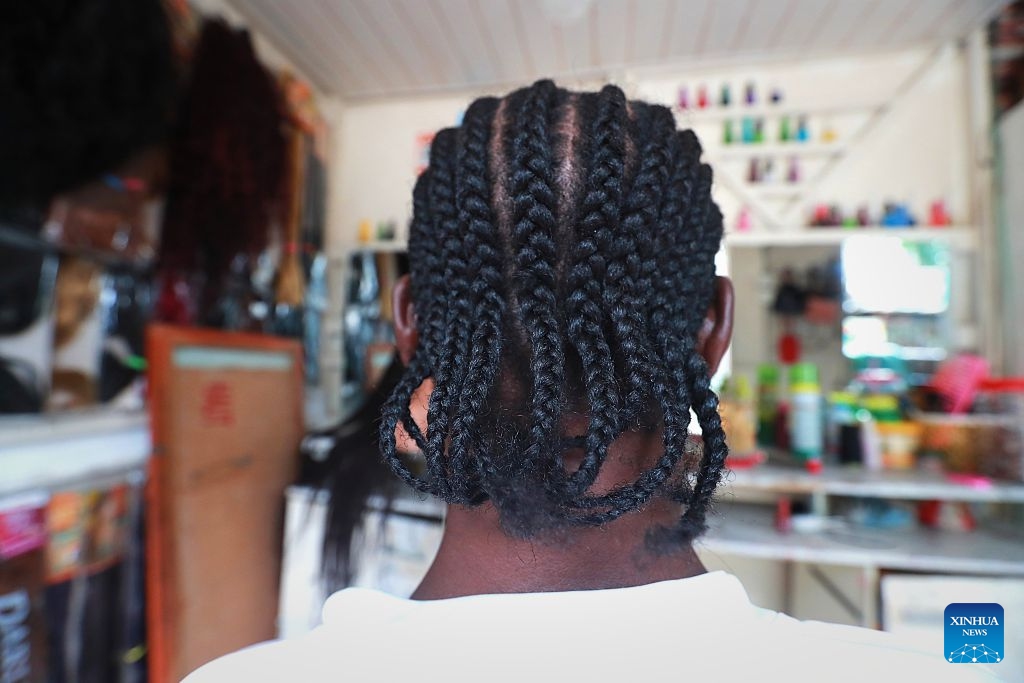 A customer shows braided hair at a street barbershop in Abidjan, Cote d'Ivoire, on July 15, 2026. Street barbershops can be found throughout Abidjan. Though often modestly equipped, they are an integral part of community life. Barbershops here also display wigs in different styles, colors and lengths, reflecting local beauty culture and strong consumer demand. More than just haircuts, these shops create jobs and offer a glimpse into the city's vibrant daily life. (Photo: Xinhua)