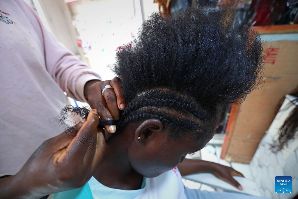 A hairstylist braids a customer's hair at a street barbershop in Abidjan, Cote d'Ivoire, on July 15, 2026. Street barbershops can be found throughout Abidjan. Though often modestly equipped, they are an integral part of community life. Barbershops here also display wigs in different styles, colors and lengths, reflecting local beauty culture and strong consumer demand. More than just haircuts, these shops create jobs and offer a glimpse into the city's vibrant daily life. (Photo: Xinhua)