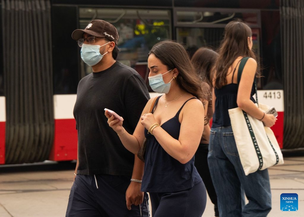 People wearing face masks walk on the street as wildfire smoke from northwestern Ontario fills the sky in Toronto, Canada, on July 15, 2026. Wildfires sweeping across northwestern Ontario, Canada, in recent days have caused severe smog and a sharp deterioration in air quality in several regions, including Ottawa, the nation's capital, and Toronto, Canada's largest city. (Photo: Xinhua)