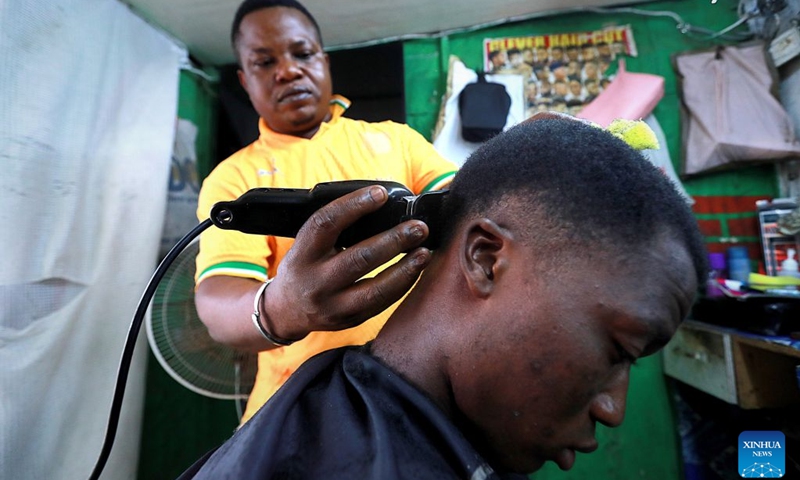 A barber shaves a customer's head at a street barbershop in Abidjan, Cote d'Ivoire, on July 15, 2026. Street barbershops can be found throughout Abidjan. Though often modestly equipped, they are an integral part of community life. Barbershops here also display wigs in different styles, colors and lengths, reflecting local beauty culture and strong consumer demand. More than just haircuts, these shops create jobs and offer a glimpse into the city's vibrant daily life. (Photo: Xinhua)