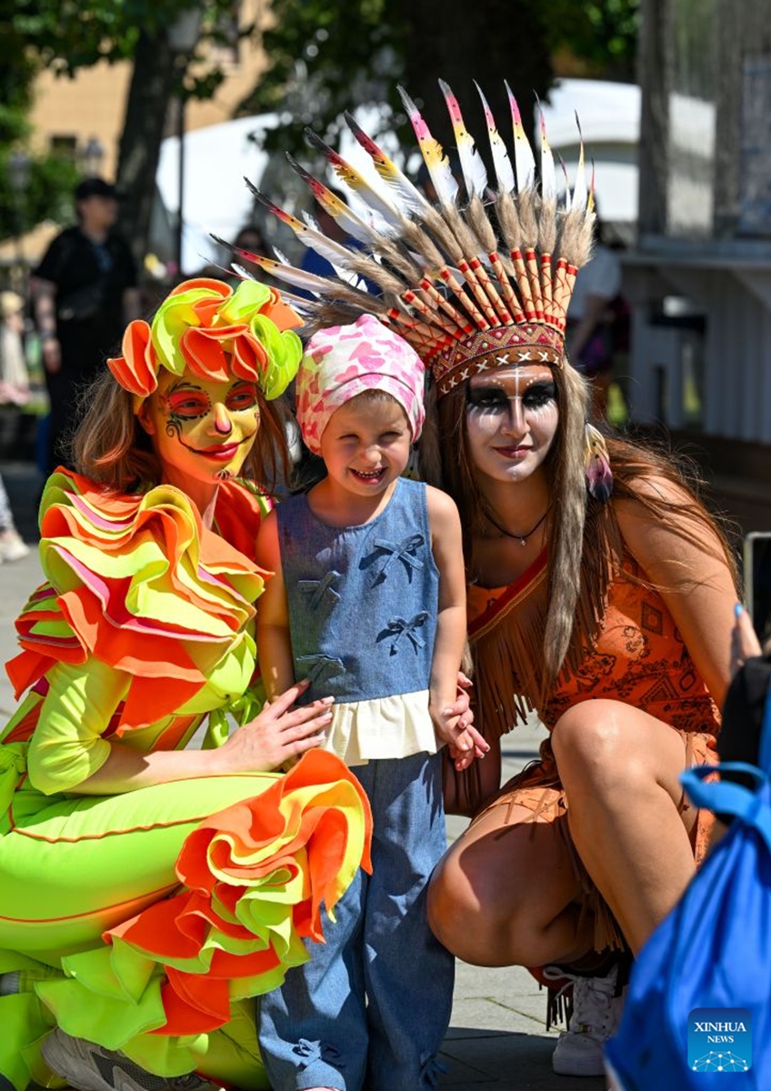 A girl poses for photos with performers during a festival of Latin American and Caribbean culture at Hermitage Garden in Moscow, Russia, July 18, 2026. Featuring live music, performance and traditional cuisines, the festival kicked off here on Saturday and will run until July 26. (Xinhua/Feng Kaihua)