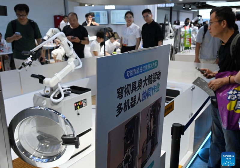 A robot opens the door of a washing machine to load clothes for laundering during the 2026 World AI Conference in Shanghai, east China, July 19, 2026. The ongoing 2026 World AI Conference turns out to be a highly competitive arena for general embodied AI products from more than 200 providers. It refers to a general-purpose intelligence system that enables robots to perform variable tasks and adapt to different application scenarios. (Xinhua/Huang Xiaoyong)