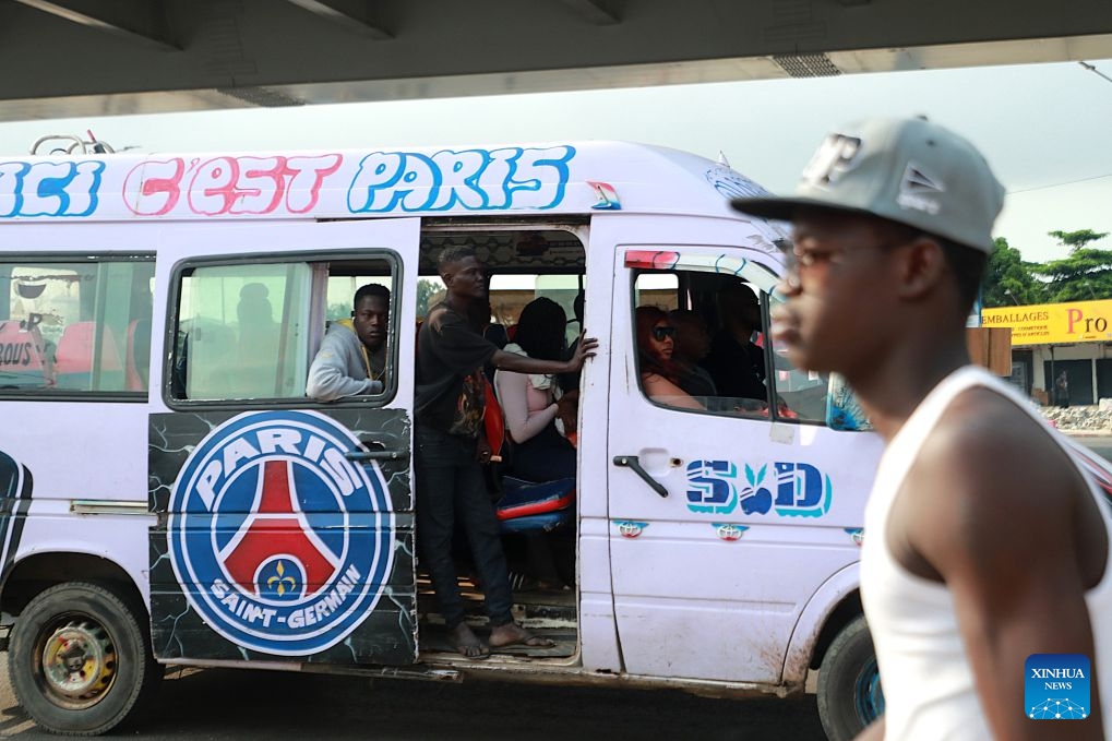 A minibus conductor (2nd L) calls for passengers in Abidjan, Cote d'Ivoire, on July 21, 2026. Colorful minibuses serve as a primary mode of transport and a vibrant element of local street culture in Abidjan, the economic capital of Cote d'Ivoire. (Photo by Yvan Sonh/Xinhua)
