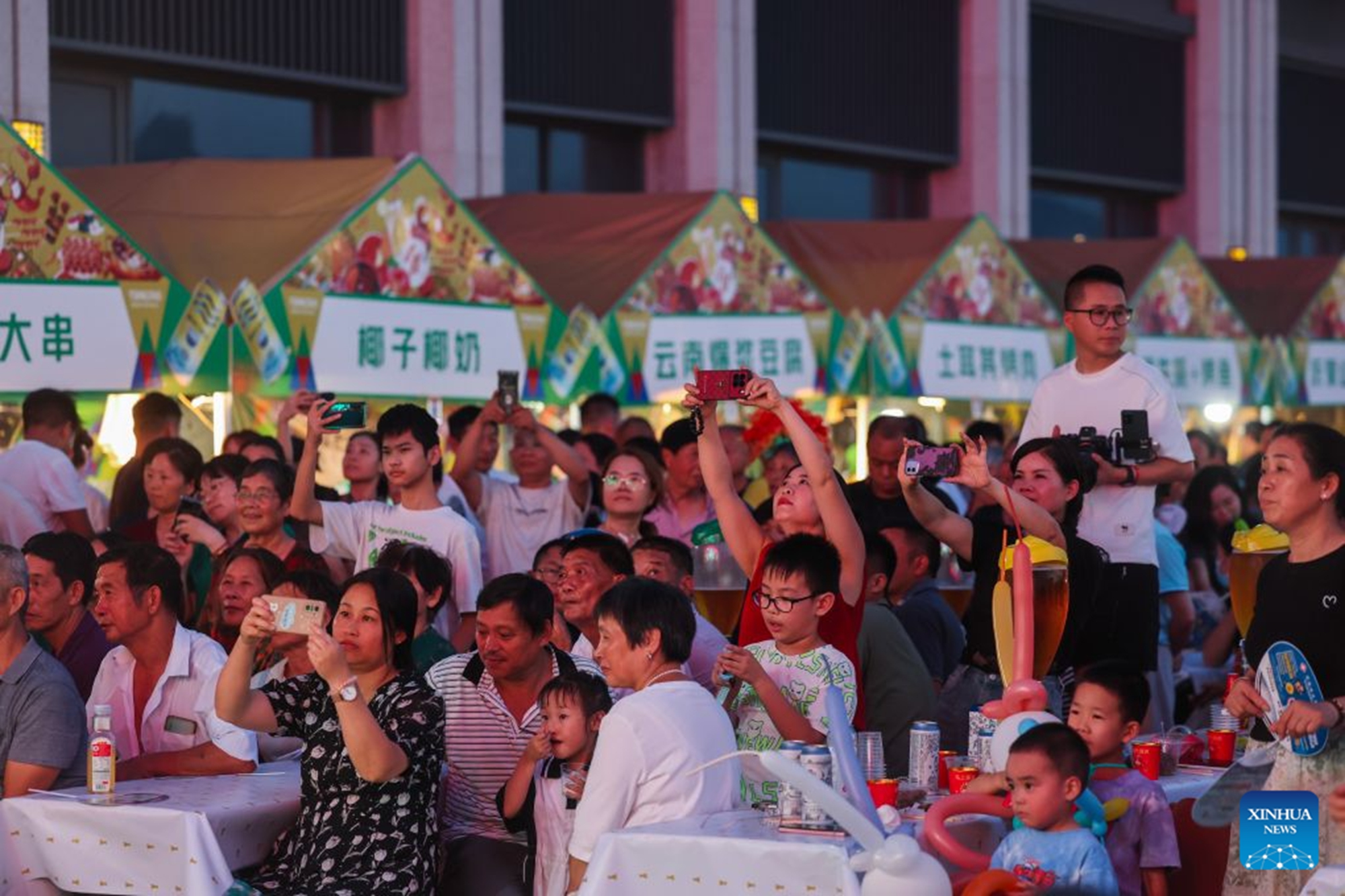 People watch a performance at a beer festival in Jiande City of east China's Zhejiang Province on July 24, 2026. A summer beer festival kicked off at a farmers market here on Friday. Featuring live performances, gourmet foods and drinks, leisure activities and bazaars, the event attracted thousands of locals and tourists. (Xinhua/Xu Yu)