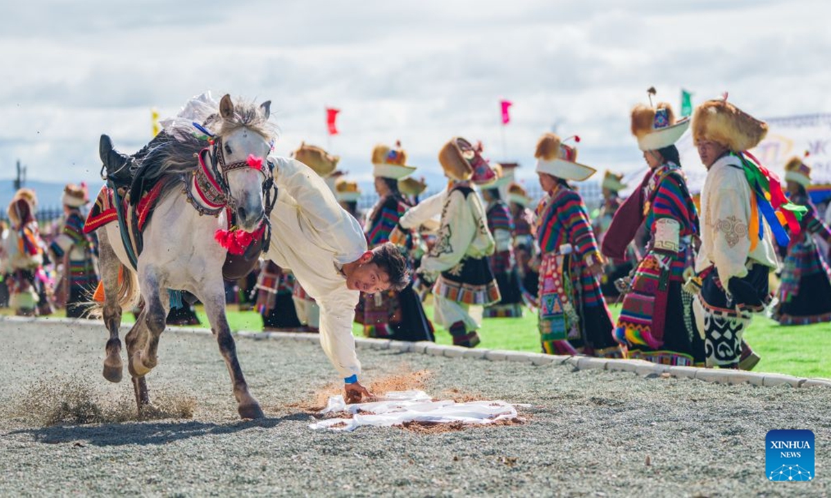 A rider performs the equestrian skill of picking hada, a traditional Tibetan silk scarf, on horseback at the opening ceremony of a horse racing competition in Amdo County, southwest China's Xizang Autonomous Region, July 23, 2026. The horse racing competition kicked off here on Thursday, featuring vibrant performances and horse racing events. (Xinhua/Tenzin Nyida)