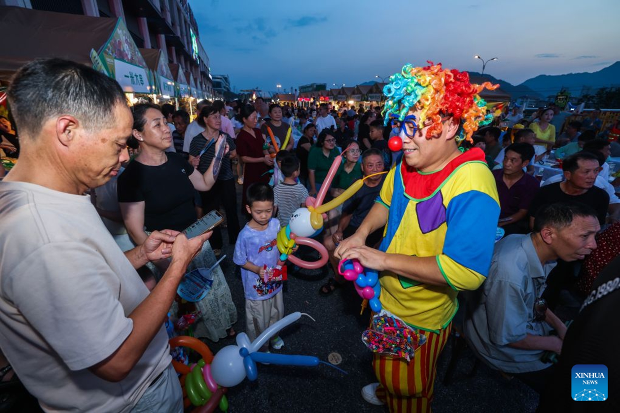 An artist interacts with visitors at a beer festival in Jiande City of east China's Zhejiang Province on July 24, 2026. A summer beer festival kicked off at a farmers market here on Friday. Featuring live performances, gourmet foods and drinks, leisure activities and bazaars, the event attracted thousands of locals and tourists. (Xinhua/Xu Yu)