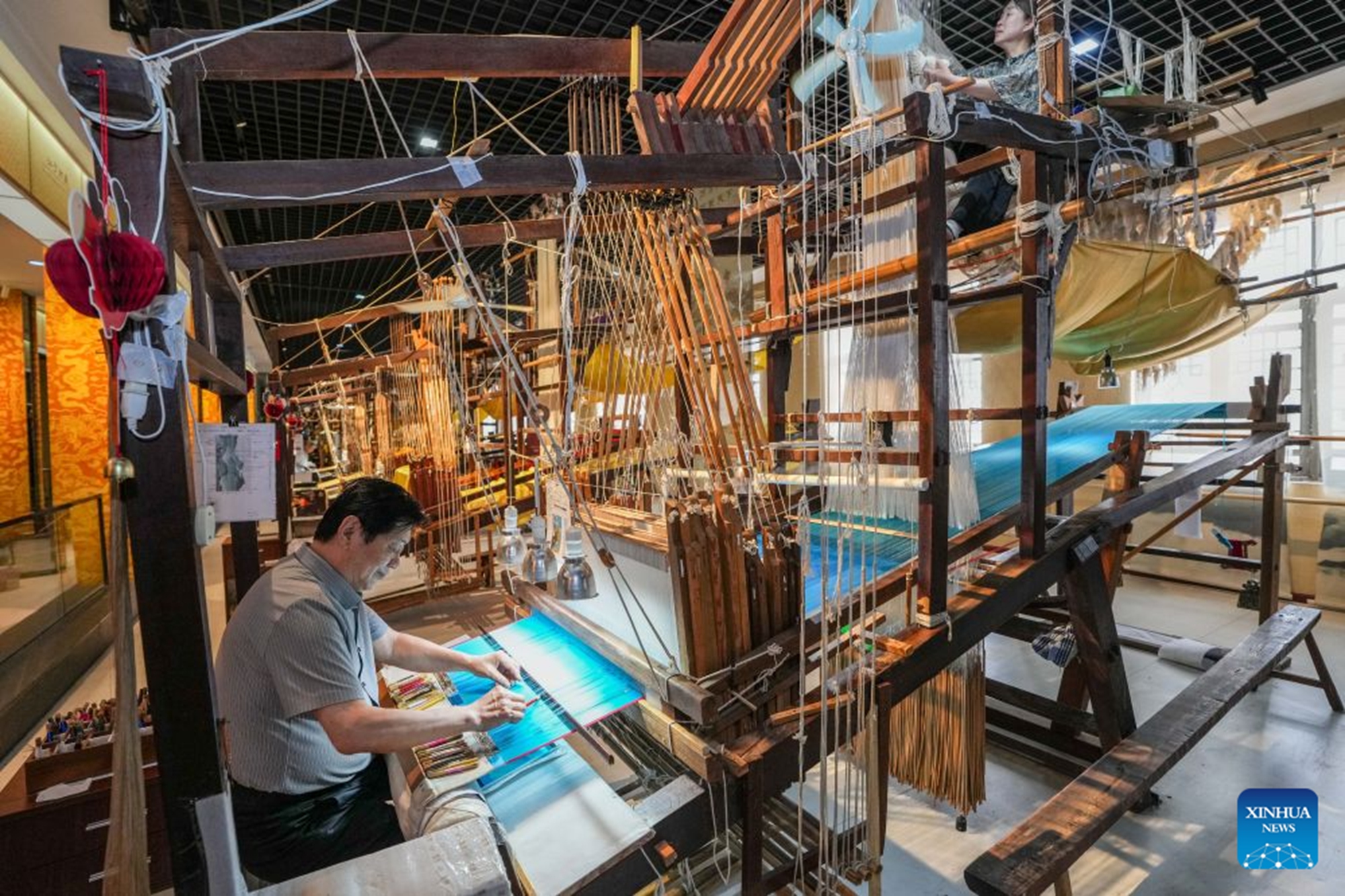 Zhou Shuangxi shows the wooden-loom Zhuanghua hand-weaving craft of Nanjing Yunjin brocade at the demonstration area of Nanjing Yunjin Brocade Museum in Nanjing, east China's Jiangsu Province, June 11, 2026. (Xinhua/Li Bo)

