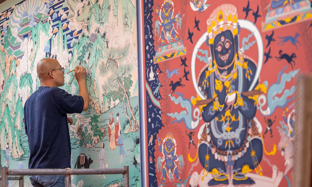A mural artist gives a live demonstration of traditional mural techniques by reproducing original murals from Qutan Temple during an exhibition at the China National Arts and Crafts Museum, also known as the China Intangible Cultural Heritage Museum, in Beijing on July 30, 2026. A Ming Dynasty (1368-1644) temple complex in Northwest China's Qinghai Province, Qutan Temple is hailed as the