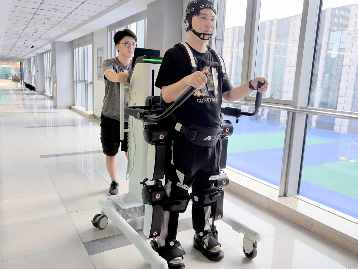 Two staff members demonstrate rehabilitation exoskeleton robot with brain-computer interface. Photo: Courtesy of Joint Laboratory for Universal AI in Disability Support