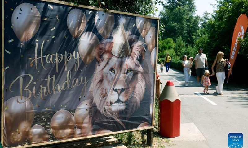 Visitors walk past a lion birthday celebration banner during an event marking the upcoming World Lion Day at Bucharest Zoo in Bucharest, Romania, Aug. 8, 2026. World Lion Day is observed on Aug. 10 every year to raise people's awareness of lion conservation. (Photo by Cristian Cristel/Xinhua)
