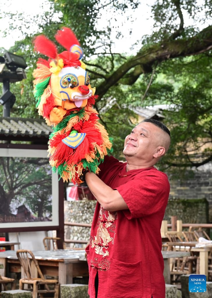 A staff member displays a hand puppet at the Yunshuiyao scenic spot, an ancient village known for its well-preserved Tulou compounds, in Nanjing County of Zhangzhou City, southeast China's Fujian Province, Aug. 20, 2026. In recent years, Nanjing County has been revitalizing its historical Tulou compounds and Hakka heritage by integrating culture and tourism, upgrading tourist attractions and introducing immersive experiences to draw more visitors. (Xinhua/Lin Shanchuan)