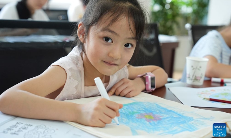 A girl draws on a canvas bag during a childcare program at a community in Ankang City, northwest China's Shaanxi Province, Aug. 20, 2026. In recent years, Ankang has been actively exploring new models of community service management for groups such as the elderly and children. (Xinhua/Shao Rui)
