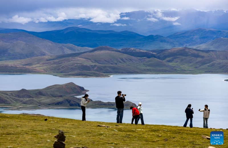 Tourists pose for photos with Lake Yamzhog Yumco, Shannan City, southwest China's Xizang Autonomous Region, Aug. 20, 2026. (Xinhua/Jiang Fan)