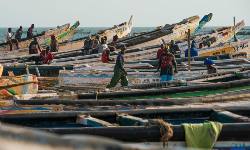 People enjoy leisure time amid traditional wooden pirogues at the Nouakchott Fishing Port in Nouakchott, Mauritania, Sept. 20, 2026. The Nouakchott Fishing Port, located on the Atlantic coast, is an important fishing hub in Mauritania. The port is known for its rows of traditional wooden pirogues and is a popular gathering place for local residents. (Xinhua/Xie Jianfei)