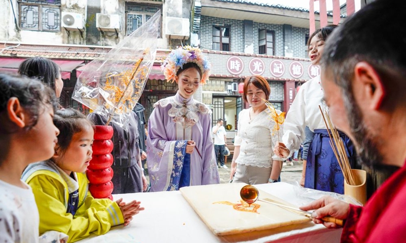 Visitors watch a candy painting performance at the ancient town of Zouma in Chongqing, southwest China, Sept. 23, 2026. As the Mid-Autumn Festival and National Day holiday period approaches, the ancient town of Zouma has launched a series of folk cultural activities, including lion dance performances, an intangible cultural heritage market, a Mid-Autumn lantern riddle fair, Hanfu experiences, and Sichuan Opera face-changing performances. Integrating the historical heritage of the town's ancient post road with contemporary folk culture experiences, these activities have attracted numerous local residents and tourists. (Xinhua/Liu Chan)