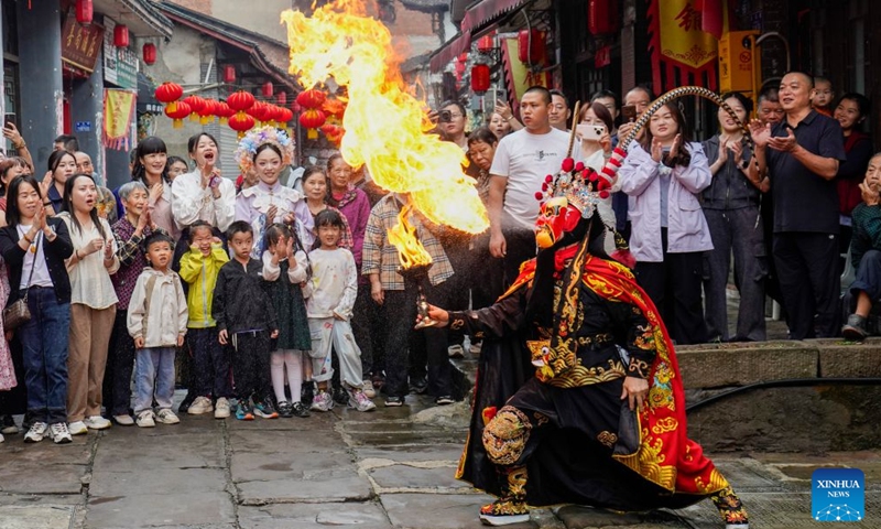 Visitors enjoy a Sichuan Opera fire-breathing performance at the ancient town of Zouma in Chongqing, southwest China, Sept. 23, 2026. As the Mid-Autumn Festival and National Day holiday period approaches, the ancient town of Zouma has launched a series of folk cultural activities, including lion dance performances, an intangible cultural heritage market, a Mid-Autumn lantern riddle fair, Hanfu experiences, and Sichuan Opera face-changing performances. Integrating the historical heritage of the town's ancient post road with contemporary folk culture experiences, these activities have attracted numerous local residents and tourists. (Xinhua/Liu Chan)