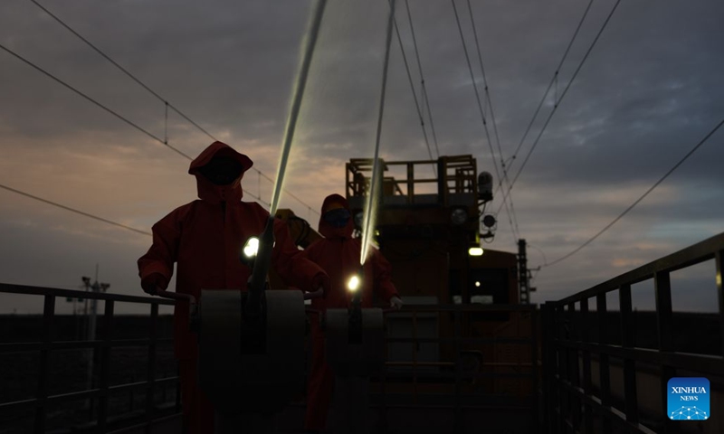 Workers carry out cleaning operations on catenary insulators in Haixi Mongolian and Tibetan Autonomous Prefecture, northwest China's Qinghai Province, Sept. 23, 2026. The Qinghai-Xizang Railway crosses Qairhan salt lake in Haixi Mongolian and Tibetan Autonomous Prefecture of northwest China's Qinghai Province. This 33-kilometer section is frequently hit by strong winds carrying salt dust, which accumulates on catenary insulators and can cause power outages. To ensure safe and reliable railway operations, workers use high-pressure washing equipment to remove salt deposits from catenary insulators along the Qairhan section. (Photo: Xinhua)