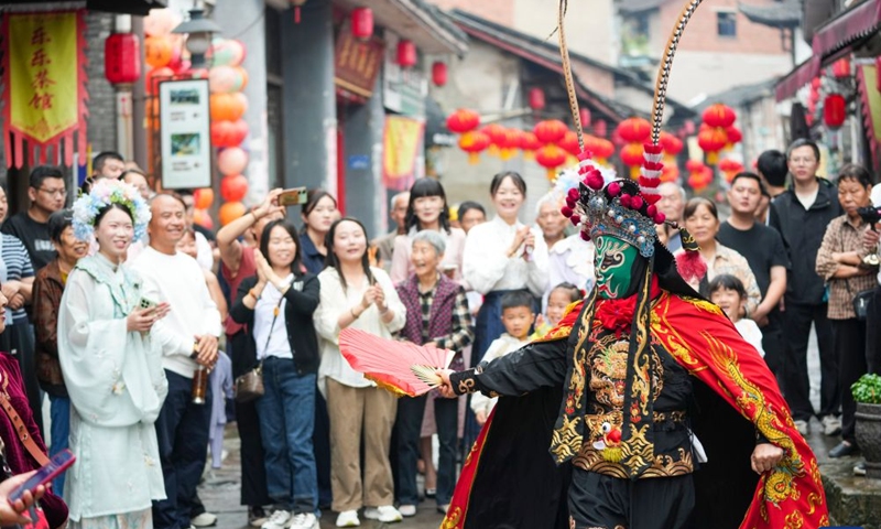 Visitors enjoy a Sichuan Opera face-changing performance at the ancient town of Zouma in Chongqing, southwest China, Sept. 23, 2026. As the Mid-Autumn Festival and National Day holiday period approaches, the ancient town of Zouma has launched a series of folk cultural activities, including lion dance performances, an intangible cultural heritage market, a Mid-Autumn lantern riddle fair, Hanfu experiences, and Sichuan Opera face-changing performances. Integrating the historical heritage of the town's ancient post road with contemporary folk culture experiences, these activities have attracted numerous local residents and tourists. (Xinhua/Liu Chan)