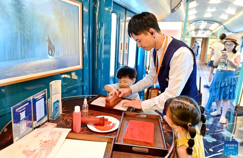 A staff member teaches children how to make traditional rubbings, an intangible cultural heritage craft, aboard the Wuyishan National Park-themed sightseeing train on Sept. 24, 2026. With the National Day holiday approaching, the Wuyishan National Park-themed sightseeing train running between Fuzhou Railway Station in southeast China's Fujian Province and Shangrao Railway Station in east China's Jiangxi Province has attracted tourists with its unique travel experience. (Xinhua/Lin Shanchuan)