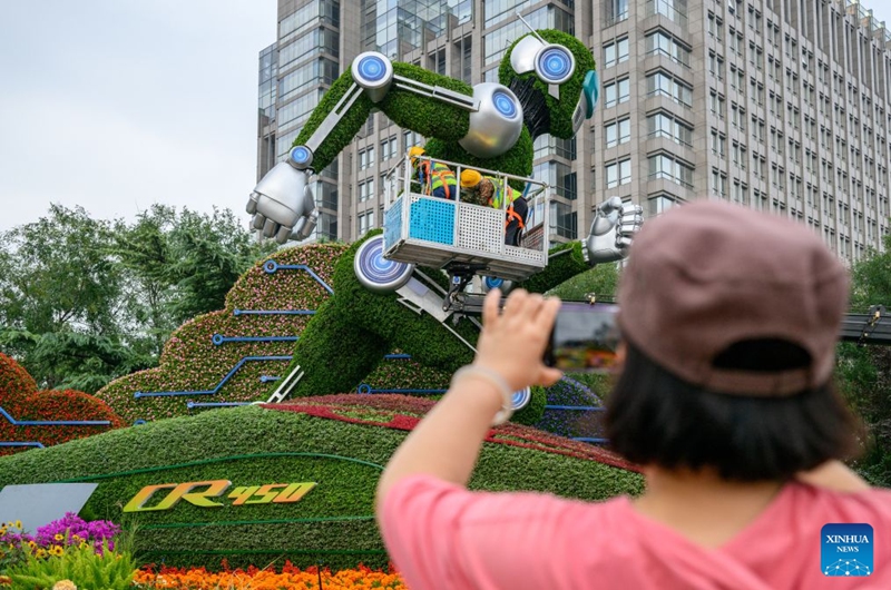 A woman takes pictures of a set of floral decorations under construction at Dongdan area along Chang'an Avenue in Beijing, capital of China, Sept. 25, 2026. Floral decorations have been set up along the Chang'an Avenue in Beijing ahead of China's National Day holidays. (Xinhua/Hu Jingwen)