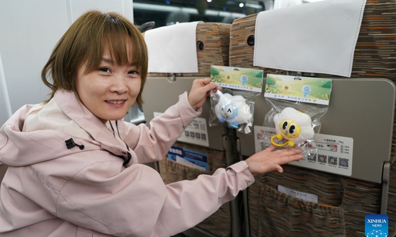 A passenger demonstrates cultural and creative products on G9997, the first train of the Xi'an-Ankang high-speed railway, in northwest China's Shaanxi Province, Sept. 28, 2026. The Xi'an-Ankang high-speed railway was officially put into operation on Monday, cutting the railway travel time between Xi'an and Ankang to less than one hour. Spanning about 171 kilometers and with a design speed of 350 kilometers per hour, the railway runs through the cities of Xi'an, Shangluo and Ankang in Shaanxi Province and has five stations along the line. (Xinhua/Shao Rui)