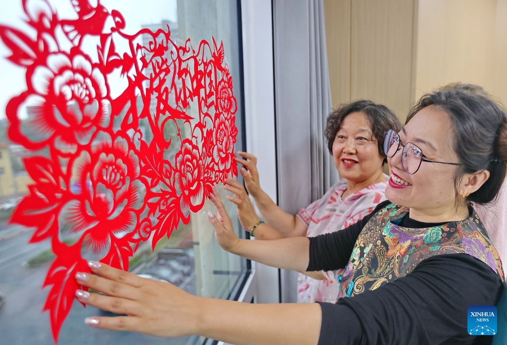 Women smooth traditional Chinese paper-cut decorations onto a glass window during an activity celebrating the upcoming National Day in Haigang District of Qinhuangdao, north China's Hebei Province, Sept. 29, 2026. Various events are held across China in celebration of the upcoming National Day. (Photo: Xinhua)