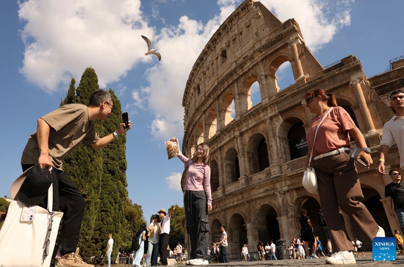 A Chinese tourist poses with a Chinese high school textbook with cover of the Colosseum in front of the Colosseum in Rome, Italy, Oct. 4, 2026. (Xinhua/Li Jing)