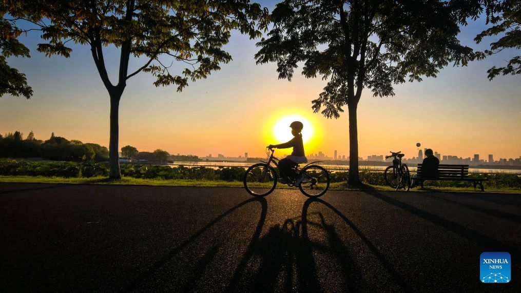 This photo taken with a mobile phone on Oct. 7, 2026 shows a tourist riding a bicycle by the East Lake at sunset in Wuhan, central China's Hubei Province. (Xinhua/Shen Hongbing)