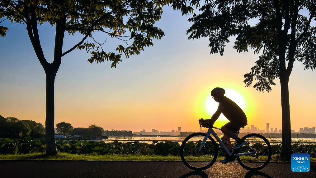 This photo taken with a mobile phone on Oct. 7, 2026 shows a tourist riding a bicycle by the East Lake at sunset in Wuhan, central China's Hubei Province. (Xinhua/Shen Hongbing)