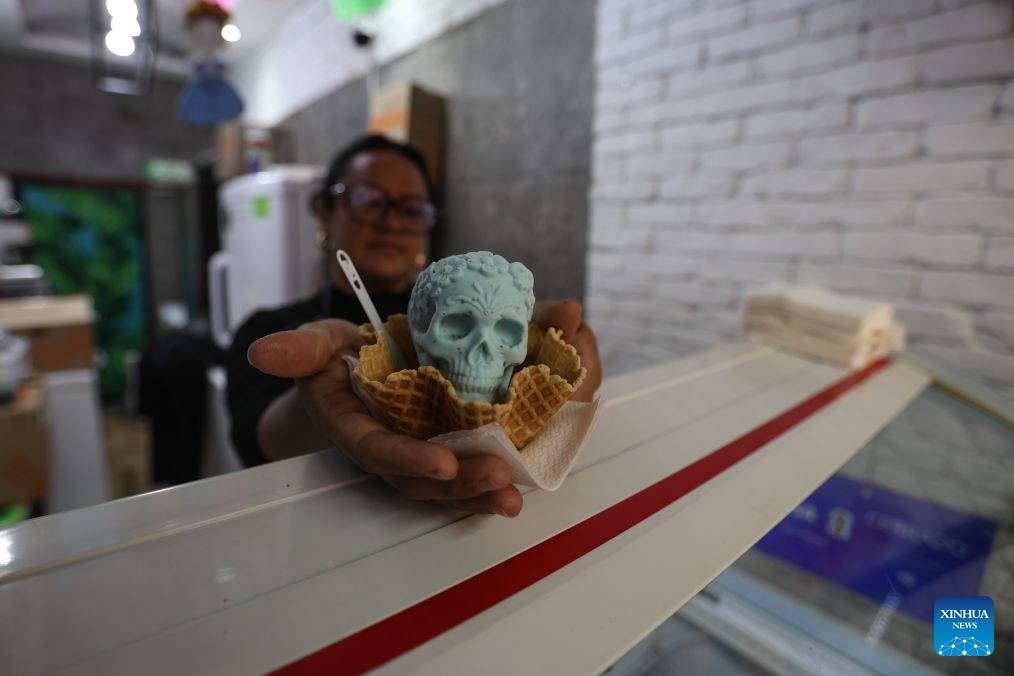 A woman hands over a Catrina-shaped ice cream in Mexico City, capital of Mexico, Oct. 17, 2026. As the Day of the Dead approaches, an ice cream shop in Mexico City has introduced Catrina-shaped ice creams, attracting many local residents and tourists. (Photo by Francisco Canedo/Xinhua)