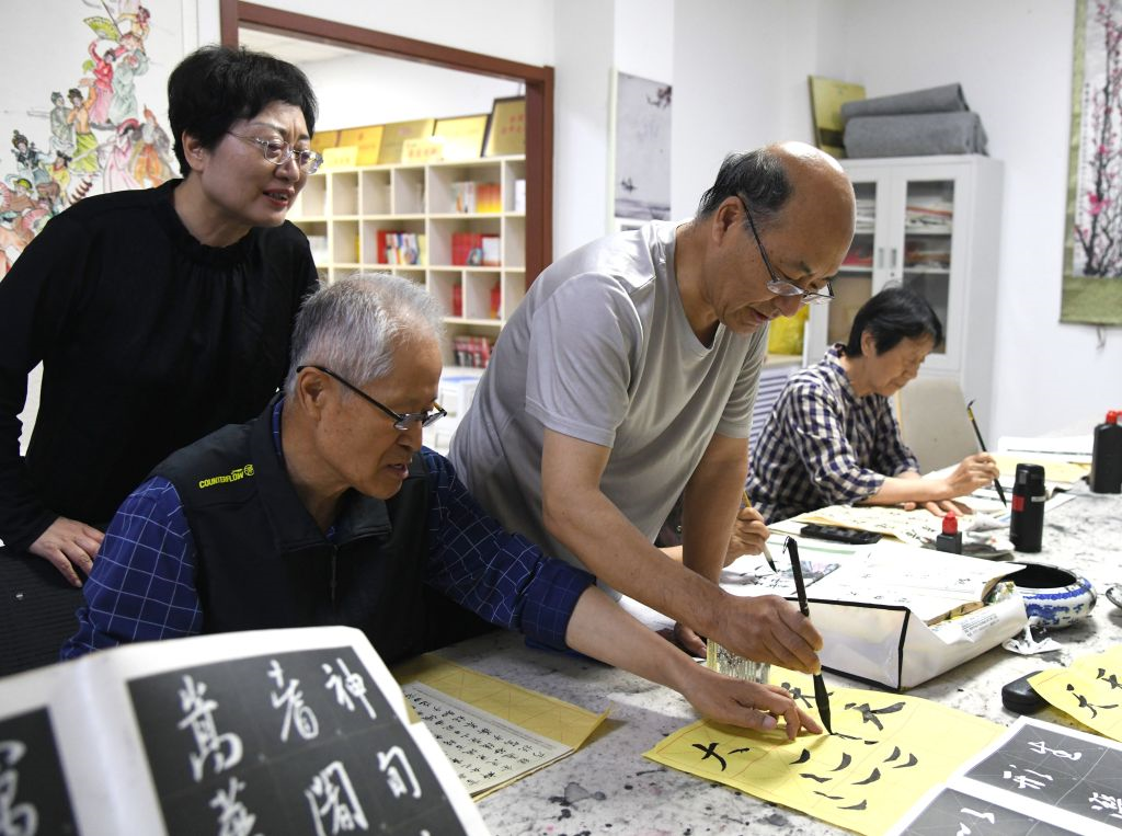 滨河社区老年志愿者（右二）给其他老人指导书法技巧。（孟瑶 摄）