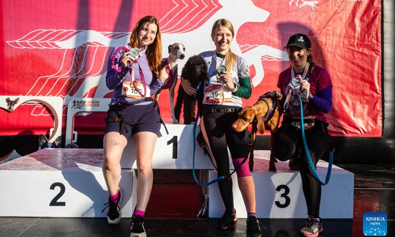 Participants pose for a photo with their dogs on the podium at the RAW PALEO Warsaw Dog Run in Warsaw, Poland, Oct. 17, 2026. Organized by the Warsaw Marathon Foundation, the event featured a roughly 5-kilometer canicross race for human-dog teams and an orienteering walk with dogs. (Photo by Jaap Arriens/Xinhua)