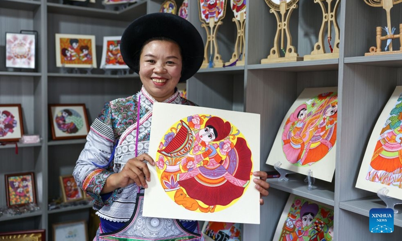 Luo Banmei, a farmer painter, displays a painting in Doujing Village of Shuicheng District in Liupanshui, southwest China's Guizhou Province, Oct. 5, 2026. In recent years, Shuicheng District has promoted its local art by offering painting training courses, establishing copyright trading platforms, and boosting the development of cultural and creative products. Shuicheng farmers' paintings are known for their bright, vibrant colors and exaggerated forms. These paintings bearing witness to local changes have become a cultural driver for rural revitalization. (Photo: Xinhua)