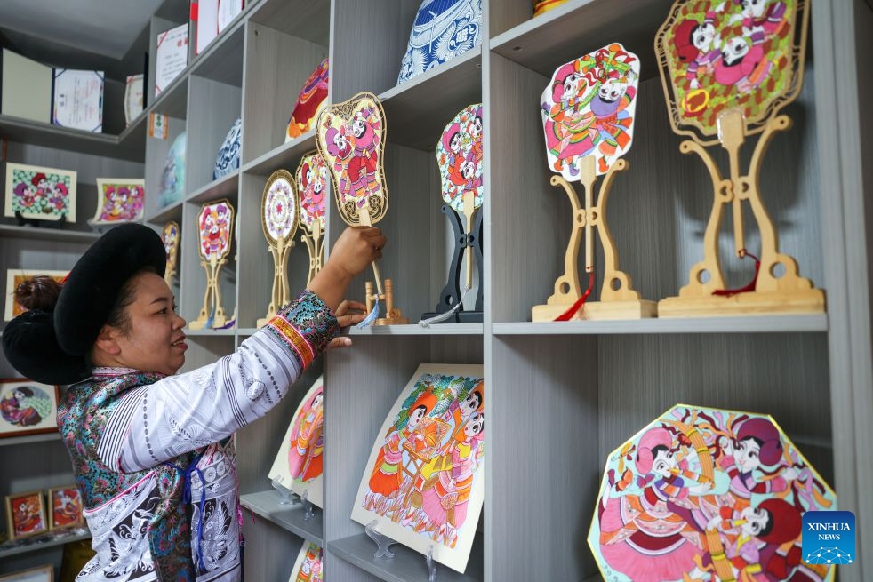 Luo Banmei, a farmer painter, arranges cultural and creative products themed on farmers' paintings in Doujing Village of Shuicheng District in Liupanshui, southwest China's Guizhou Province, Oct. 5, 2026. In recent years, Shuicheng District has promoted its local art by offering painting training courses, establishing copyright trading platforms, and boosting the development of cultural and creative products. (Photo: Xinhua)