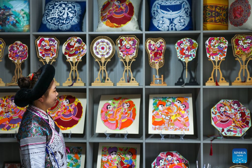 Luo Banmei, a farmer painter, looks at cultural and creative products themed on farmers' paintings in Doujing Village of Shuicheng District in Liupanshui, southwest China's Guizhou Province, Oct. 5, 2026. In recent years, Shuicheng District has promoted its local art by offering painting training courses, establishing copyright trading platforms, and boosting the development of cultural and creative products. (Photo: Xinhua)