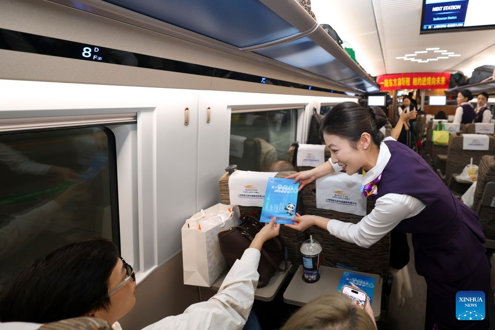 A staff member hands a brochure on China International Import Expo (CIIE) to a passenger during an activity promoting the upcoming 9th CIIE on the train G901, Oct. 28, 2026. A promotion activity was held on the train G901 on Wednesday to show highlights of this year's CIIE, which will be held in Shanghai from Nov. 5 to 10. (Xinhua/Wang Xiang)