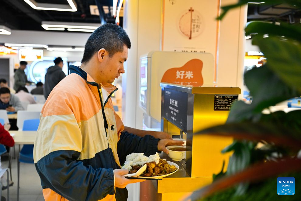 A customer takes a bowl of soup from a machine at the AI Mirror World Restaurant in Nanjing, east China's Jiangsu Province, Oct. 26, 2026. With a human-machine collaborative operation model, the restaurant makes some of its meals and drinks through standardized production powered by AI kitchen equipped with smart noodle and beverage making machines. (Xinhua/Ji Chunpeng)