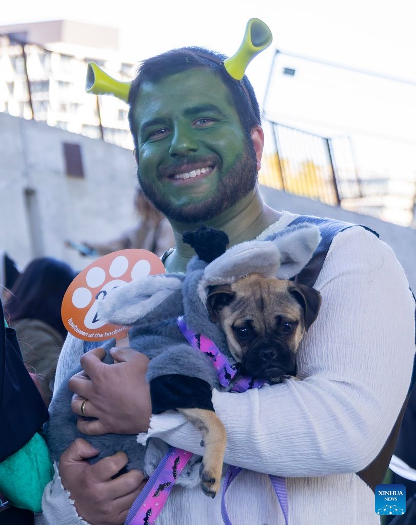 A dog and its owners pose for photos during Howl'oween at the Bentway, a dog-and-owner costume contest, in Toronto, Canada, on Oct. 24, 2026. The annual event was held here on Saturday, bringing Halloween fun for dogs and their owners. (Photo by Zou Zheng/Xinhua)