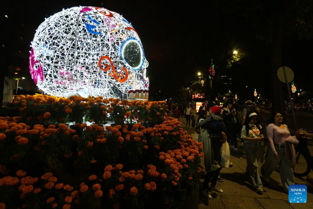 People walk past a skull-shaped light art installation surrounded by marigolds along Paseo de la Reforma in Mexico City, capital of Mexico, Oct. 23, 2026. As the Day of the Dead approaches, giant light sculptures along Paseo de la Reforma in Mexico City, capital of Mexico, are illuminated. (Photo by Francisco Canedo/Xinhua)